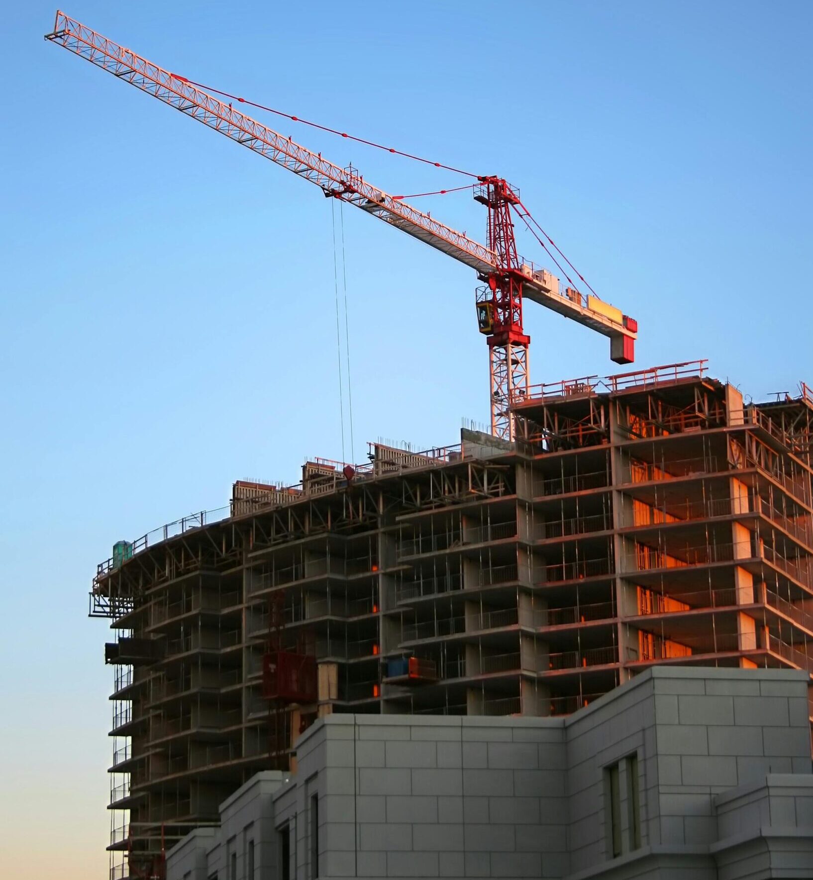 Tower crane on a high-rise building under construction at sunset, showcasing modern urban development.